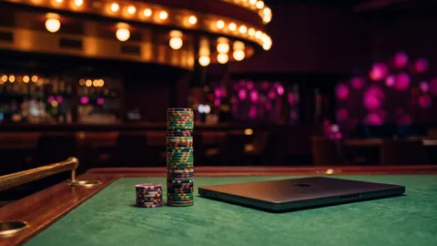 A tall and a short stack of casino chips on green baize beside a closed laptop