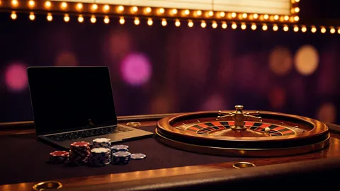 Small roulette wheel next to a laptop and a stack of casino chips